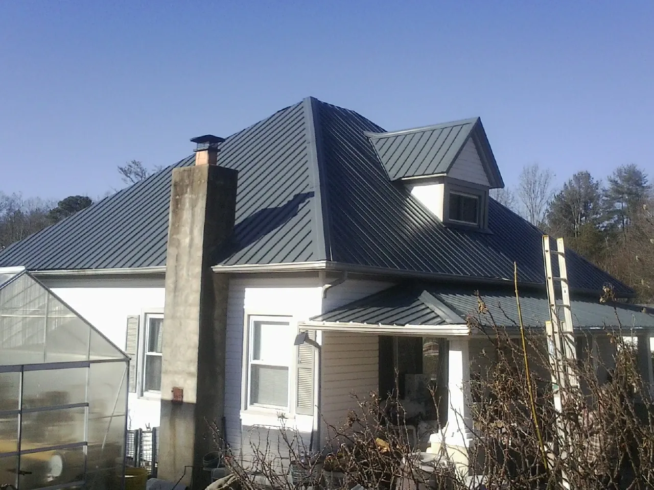 Dark blue standing seam metal roof on a white farmhouse with dormer — Slate & Tile Roof Repair by Roofing Brothers in West Oneonta