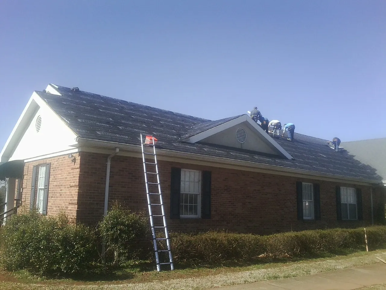 Crew tearing shingles off a brick ranch roof with a ladder set — Metal Roof Repair work by our crew in West Oneonta