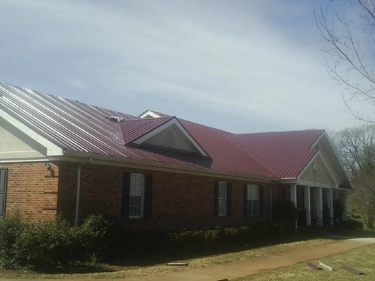 Red metal roof with gabled entries on a long brick building, from a Hail Damage Roof Repair job in West Oneonta