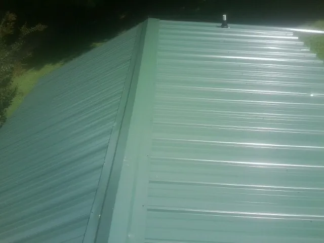 New green metal panels meeting at the ridge of a roof — Flat Roof Repair work by our crew in West Oneonta