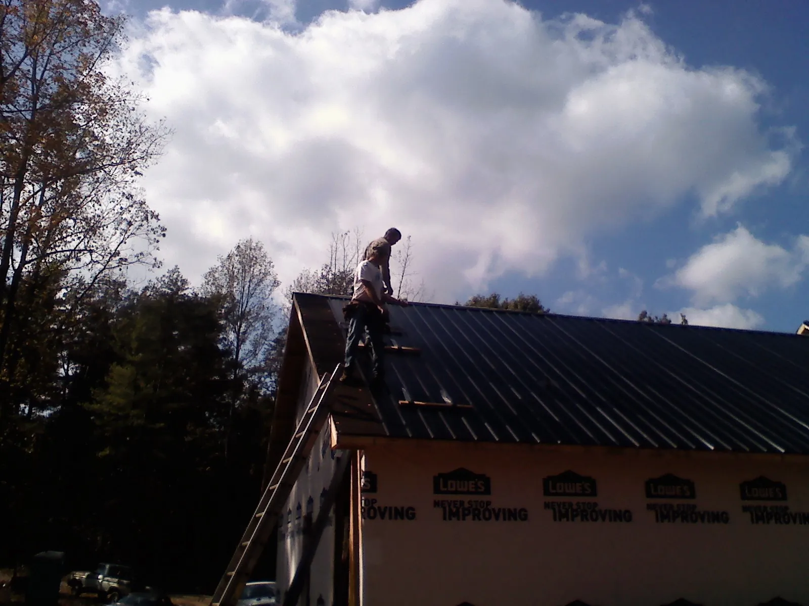 Roofer fastening dark metal panels high against a cloudy sky, from a Roof Inspection job in West Oneonta