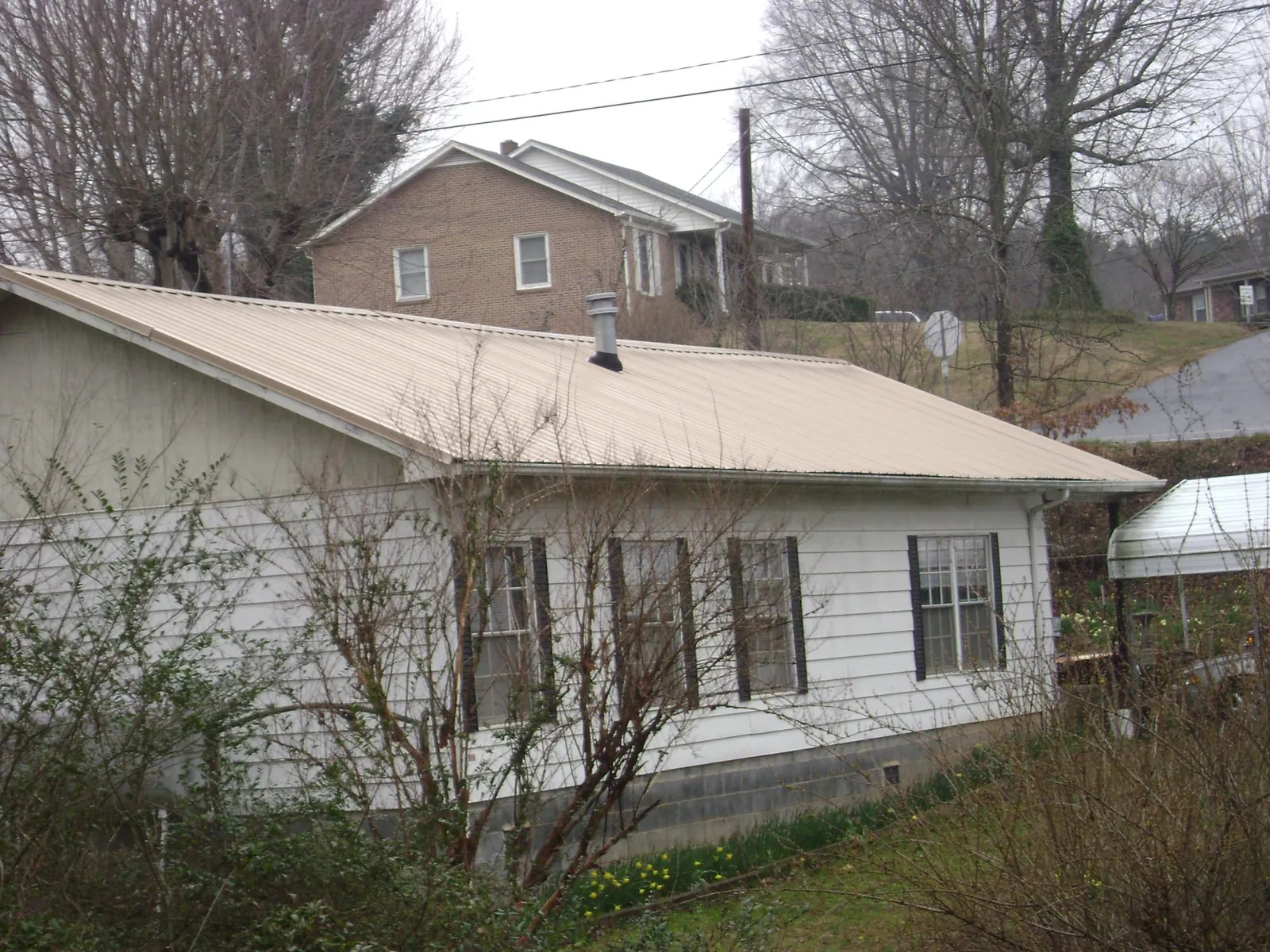 Tan metal roof on a white sided house set into a hillside — Commercial Roofing by Roofing Brothers in West Oneonta