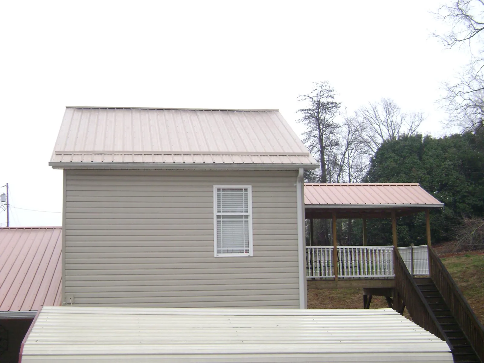 Tan metal roofs on a two story addition and attached porch, from a Roof Replacement job in West Oneonta